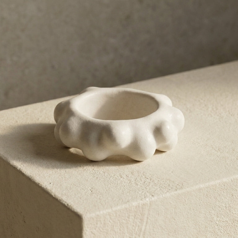 Burbuja — anillo de porcelana blanca con fila de esferas sobre repisa de piedra beige con luz lateral
