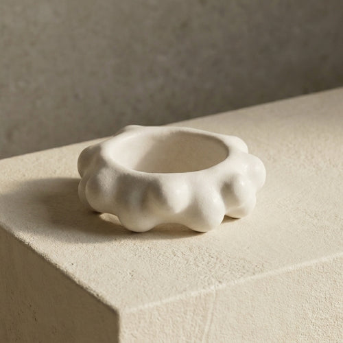 Burbuja — anillo de porcelana blanca con fila de esferas sobre repisa de piedra beige con luz lateral
