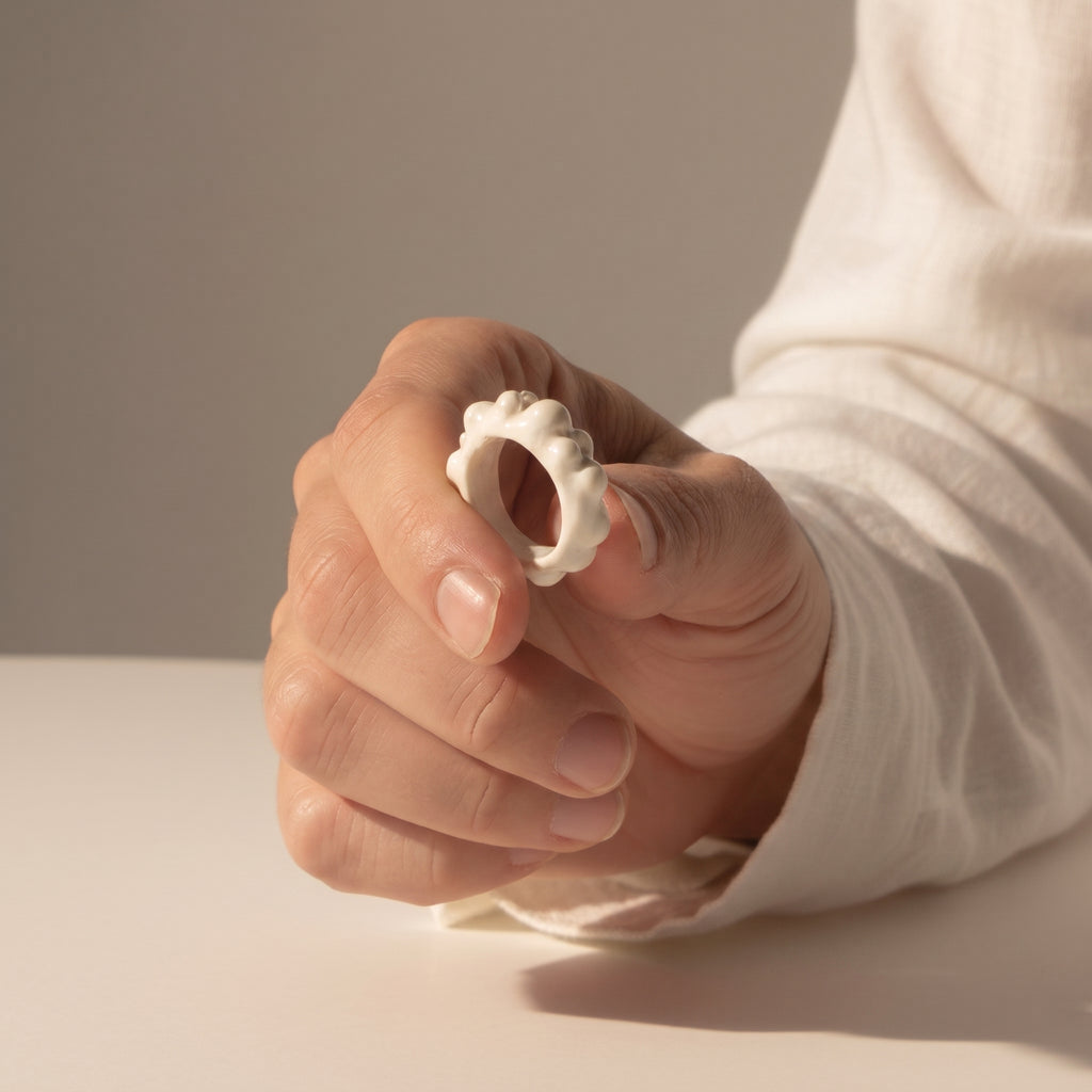 Burbuja — anillo de porcelana blanca con fila de esferas en mano cerrada con camisa blanca