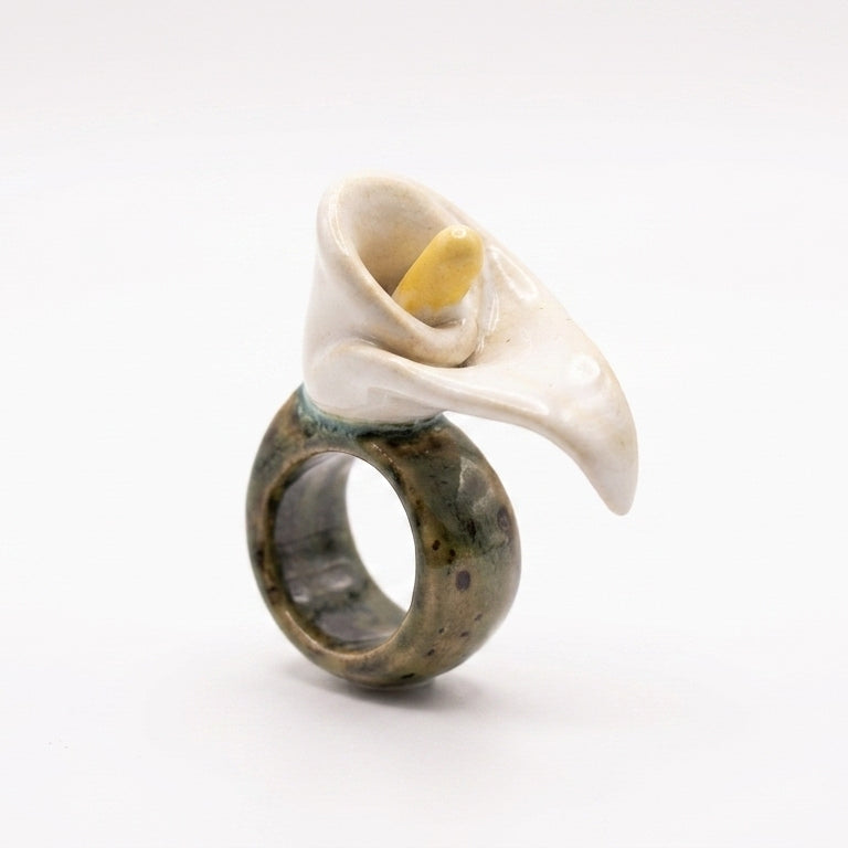 Cala — anillo de porcelana con flor de cala blanca sostenido entre dedos con luz solar lateral