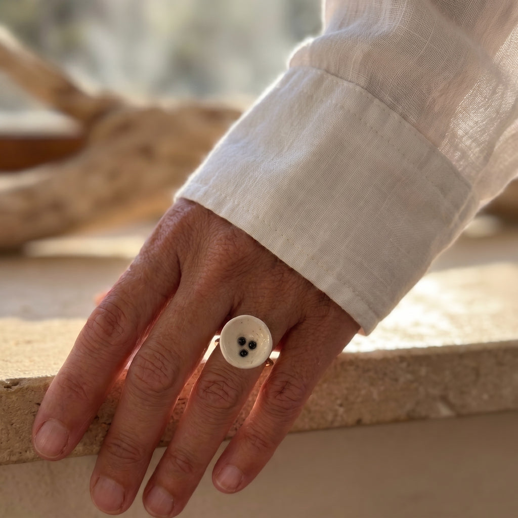 Nidus — anillo de porcelana con puntos negros en mano, luz natural