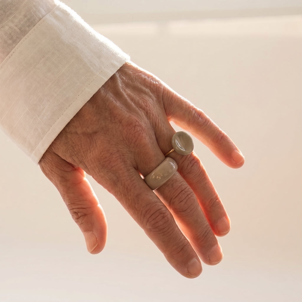 Nidus Topo — anillo de porcelana topo brillante combinado con anillo de porcelana beige en mano alzada con camisa lino, luz dorada de atardecer sobre fondo beige
