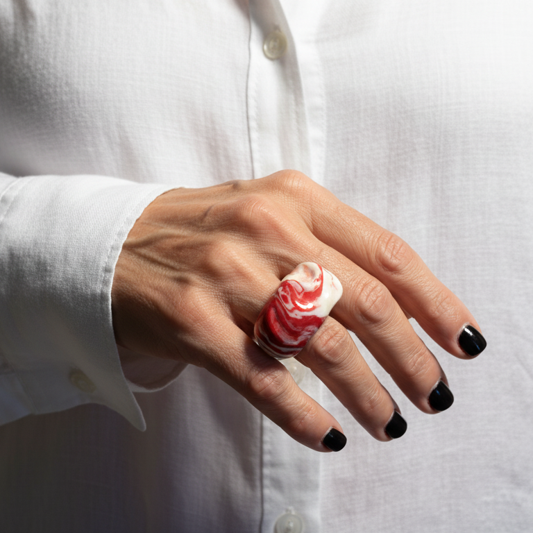 Petra Surco Rouge — anillo de porcelana marmolada rojo y blanco en mano con uñas rojas apoyada en camisa blanca