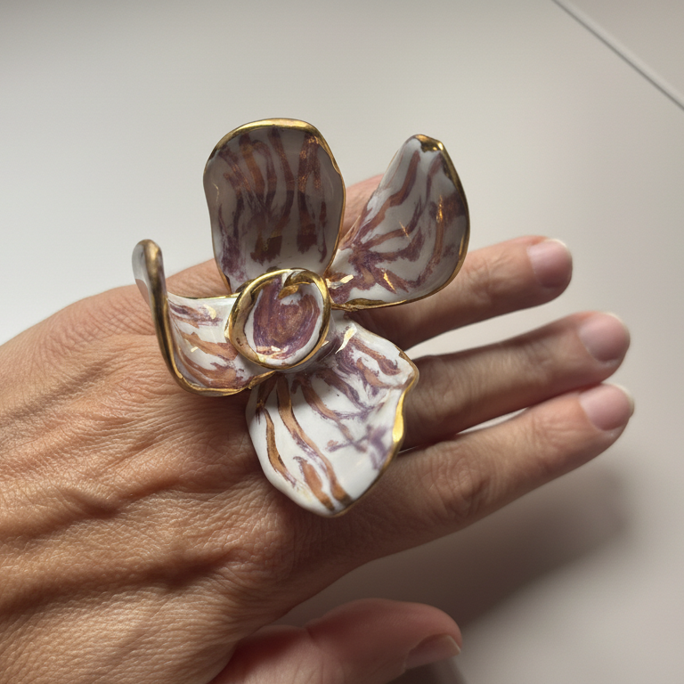 Jazmín Dorado — anillo flor de porcelana blanca con vetas lila y bordes dorados en mano abierta sobre superficie blanca