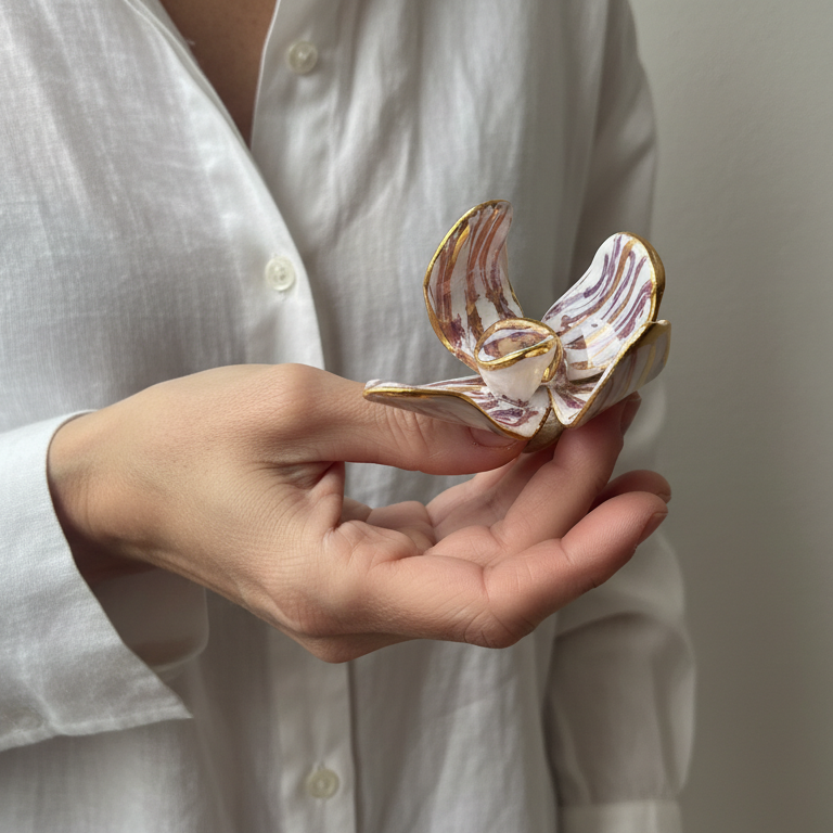 Jazmín Dorado — anillo flor de porcelana blanca con vetas lila y bordes dorados sostenido en palma de mano con camisa lino