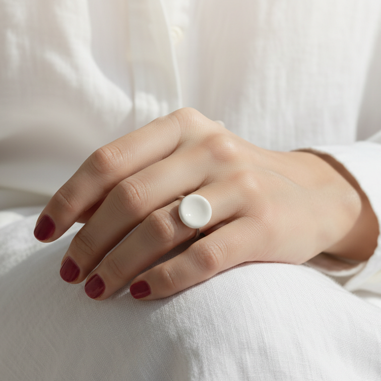 Nidus Blanco — anillo de porcelana blanca cóncava en mano apoyada sobre superficie beige con camisa blanca, vista lateral