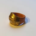 Crépité — anillo de barro terracota con cúpula de oro craquelado, vista lateral sobre fondo blanco mostrando contraste terracota y oro