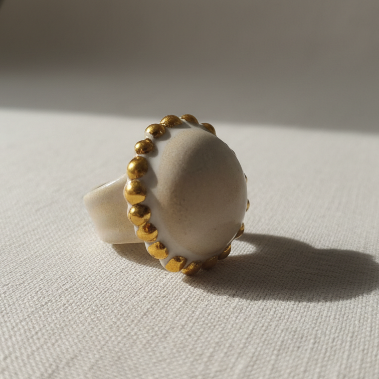 Sol de Invierno — anillo de porcelana blanca mate con orla de bolitas de oro sobre superficie de lino blanco con luz solar lateral, vista frontal