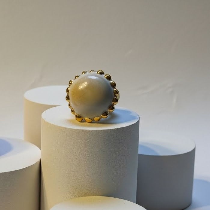 Sol de Invierno — anillo de porcelana blanca mate con orla de bolitas de oro sobre pedestales blancos de distintas alturas, vista frontal con fondo gris suave
