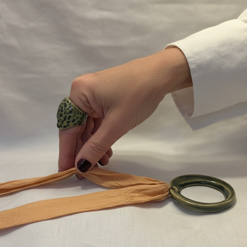 Áspid Anillo — anillo de porcelana con cúpula rugosa en esmalte verde musgo con manchas turquesa en mano con uñas burdeos y camisa blanca, fondo gris neutro