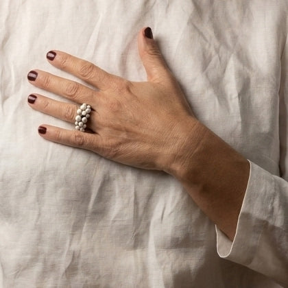 Burbujas Black — anillo de porcelana negra con esferas blancas apiladas en mano apoyada sobre tela lino blanca arrugada, vista cenital con luz suave