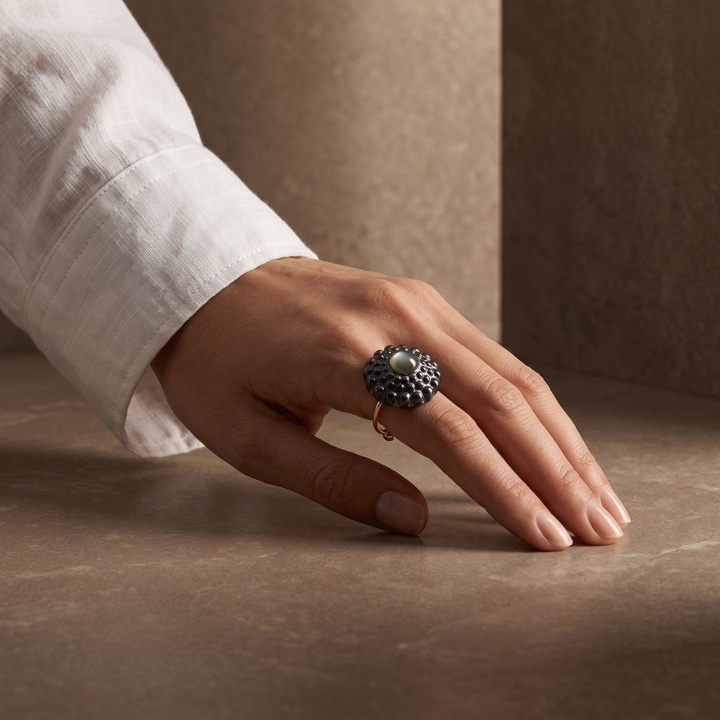 Girándola Azul Nacarado — mano femenina con camisa blanca apoyada sobre superficie beige, vista alternativa del anillo azul nacarado