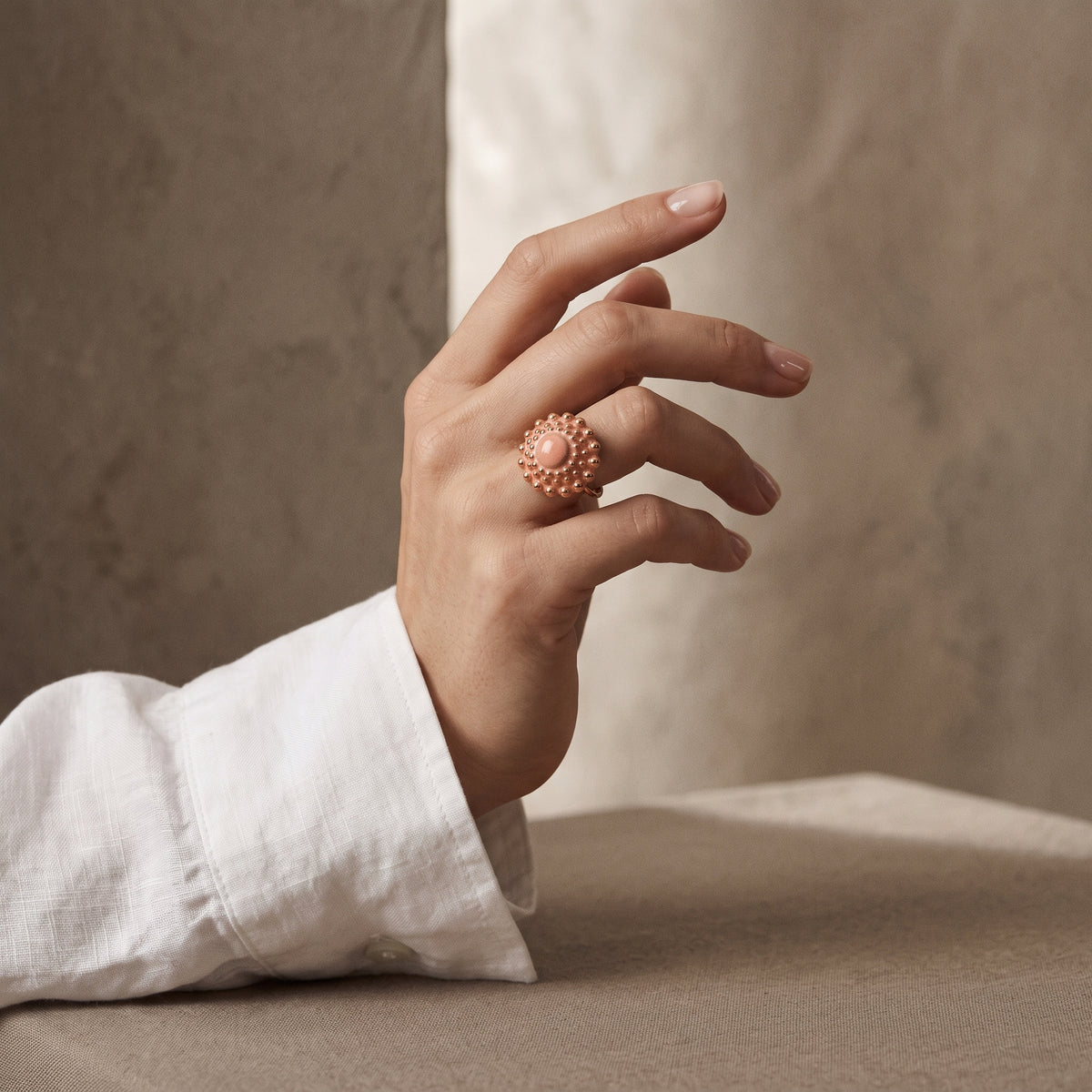 Girándola Rosa Palo — anillo de porcelana rosa cálido con bultos dorados en mano femenina con camisa blanca, fondo beige con pilar de mármol