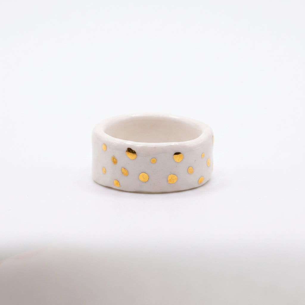 Polvo de Estrella — anillo de porcelana blanca mate con puntos de oro brillante distribuidos irregularmente, vista frontal sobre fondo blanco