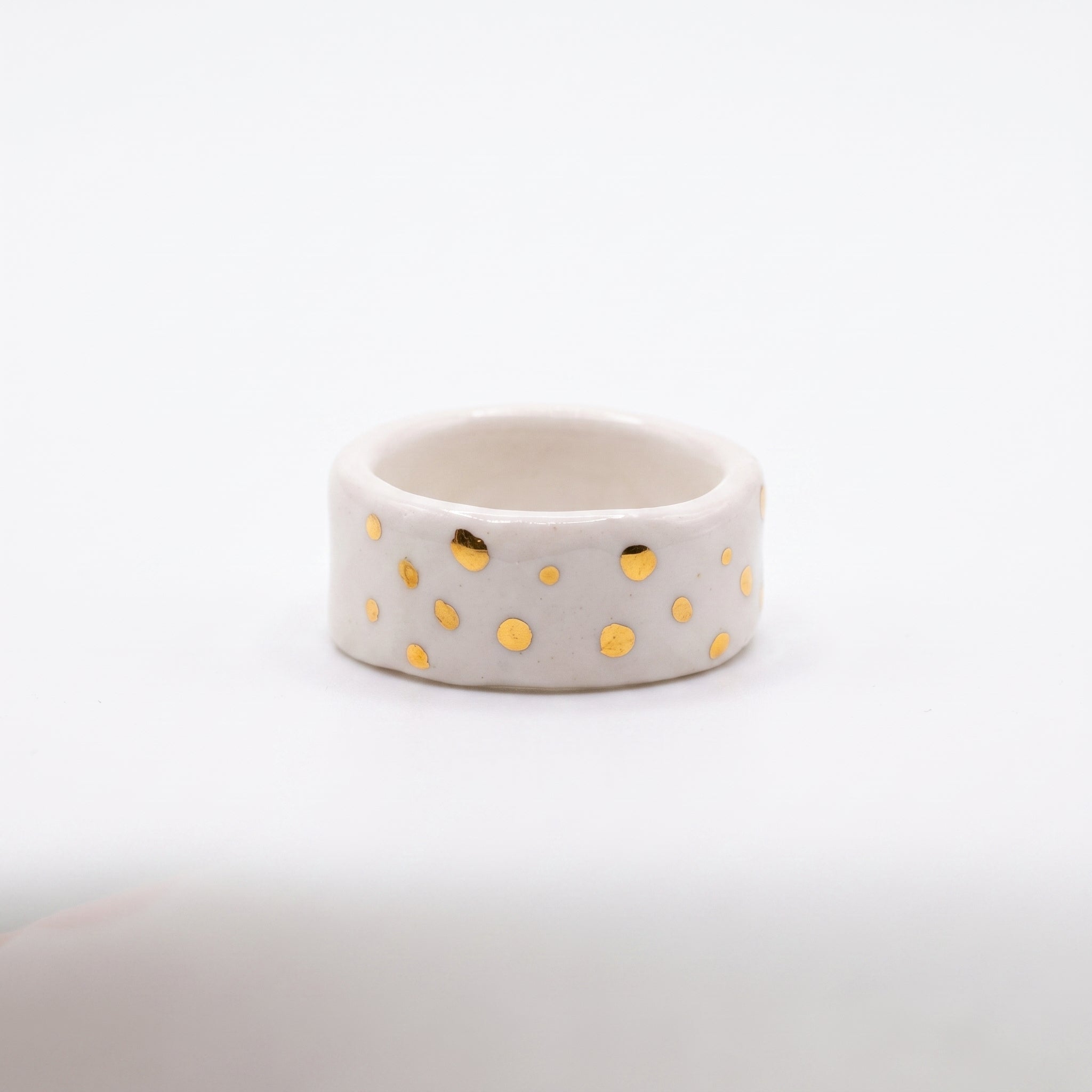 Polvo de Estrella — anillo de porcelana blanca mate con puntos de oro brillante distribuidos irregularmente, vista frontal sobre fondo blanco