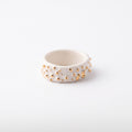 Polvo de Estrella Relieve — anillo de porcelana blanca mate con pirámides y conos en relieve rematados en oro brillante distribuidos irregularmente, vista frontal sobre fondo blanco