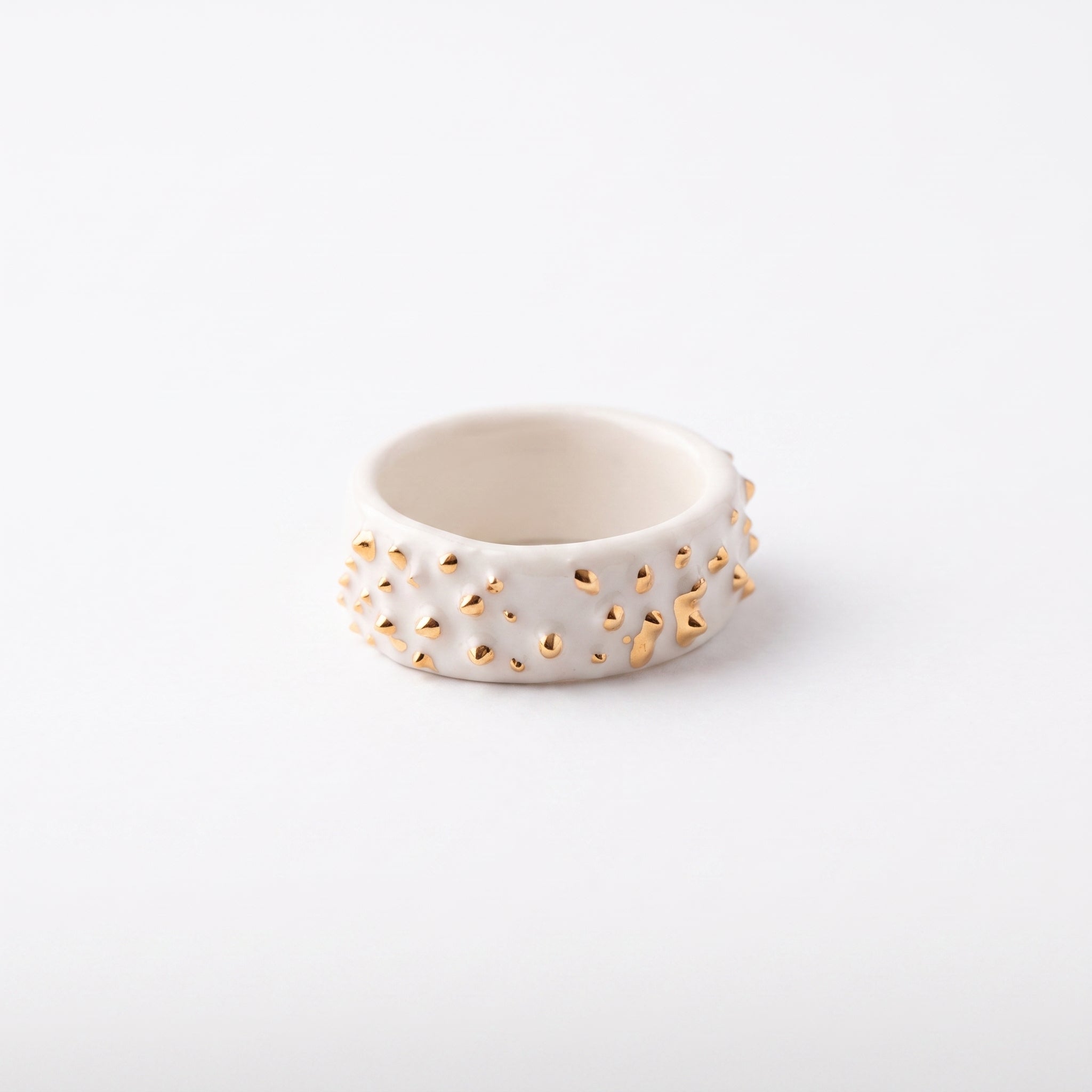 Polvo de Estrella Relieve — anillo de porcelana blanca mate con pirámides y conos en relieve rematados en oro brillante distribuidos irregularmente, vista frontal sobre fondo blanco