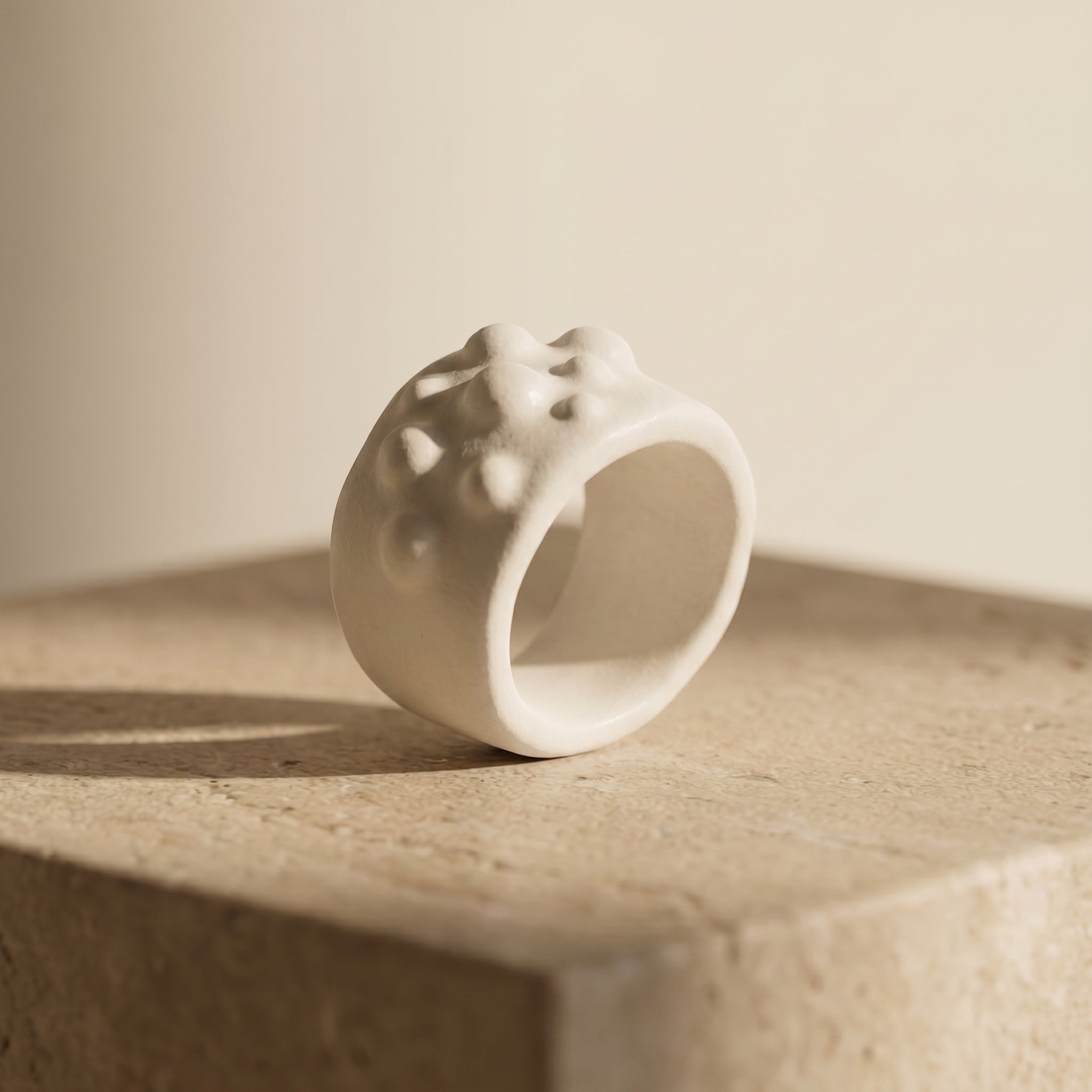 Bulla — anillo de porcelana blanca con textura de burbujas sobre piedra travertino