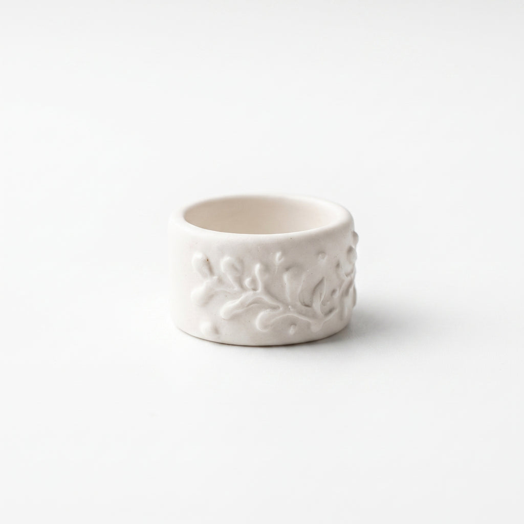 Orla — anillo de porcelana blanca mate con ramas y hojas en relieve cubriendo toda la superficie, vista frontal sobre fondo blanco