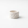 Orla — anillo de porcelana blanca mate con ramas y hojas en relieve cubriendo toda la superficie, vista frontal sobre fondo blanco