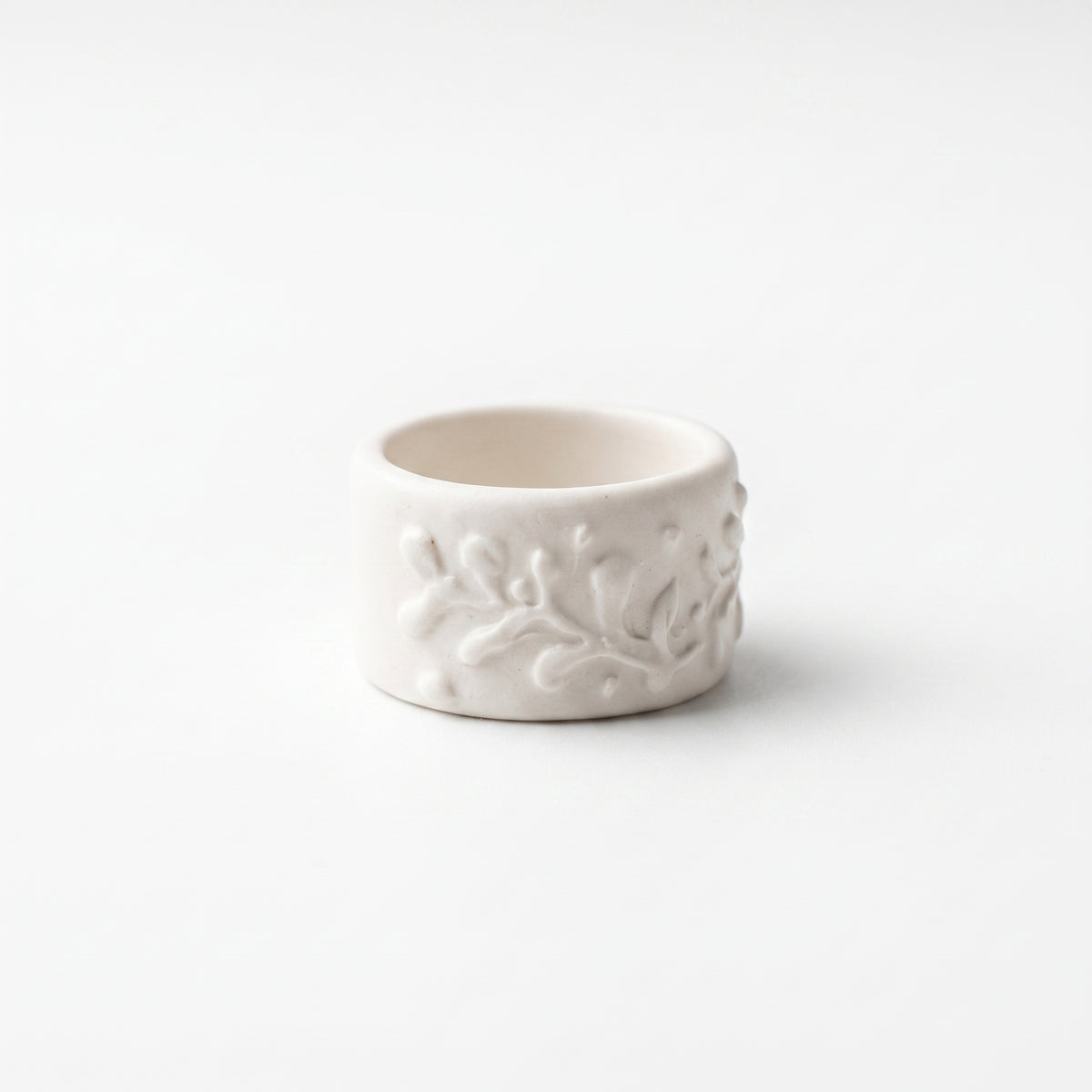 Orla — anillo de porcelana blanca mate con ramas y hojas en relieve cubriendo toda la superficie, vista frontal sobre fondo blanco