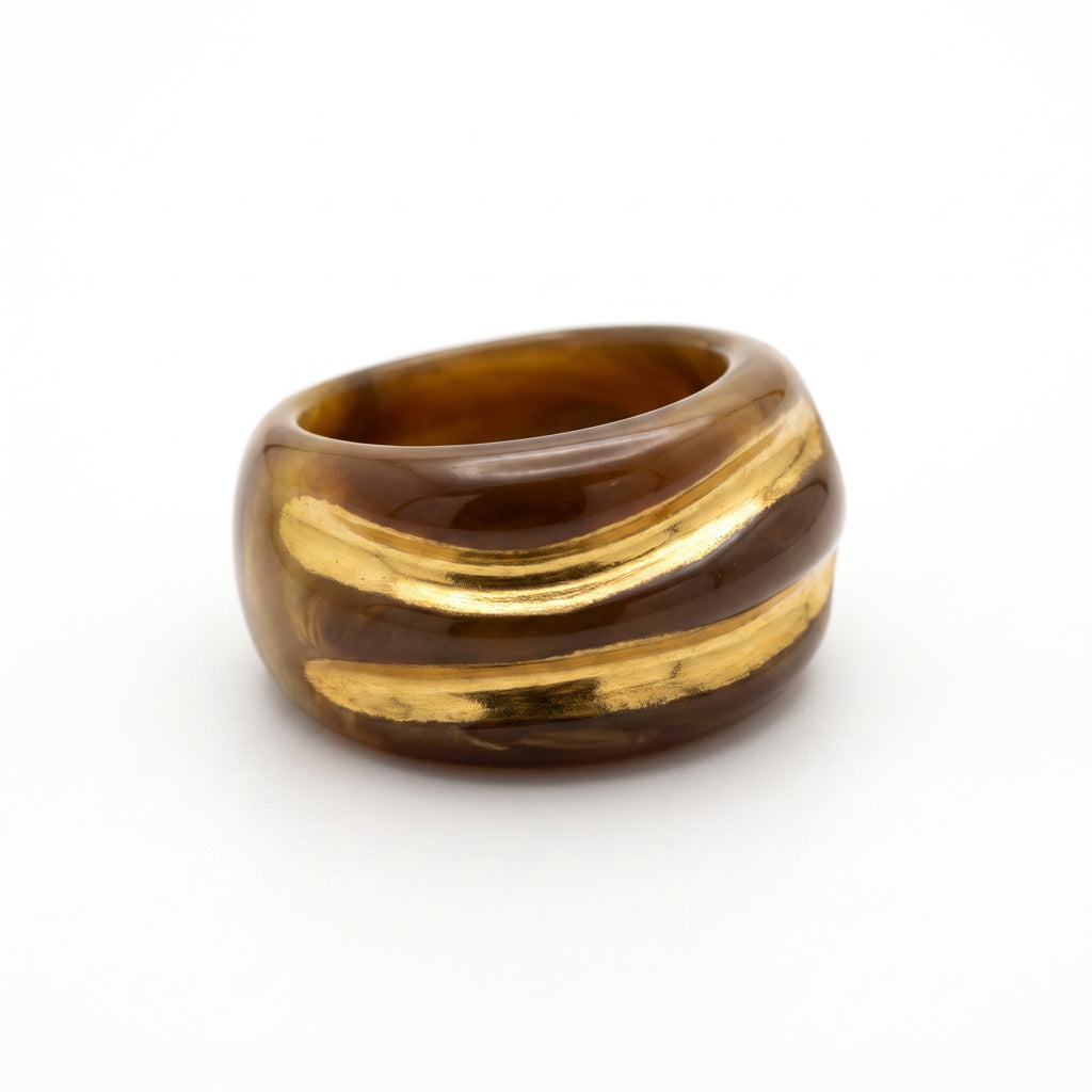 Onda Caramelo — anillo de porcelana con esmalte caramelo brillante y vetas doradas en mano apoyada sobre otra mano, luz solar cálida con sombras dramáticas sobre fondo oscuro
