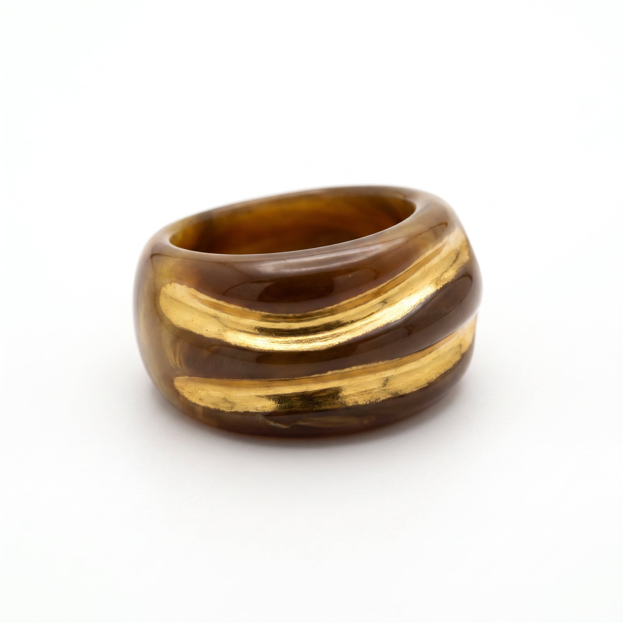 Onda Caramelo — anillo de porcelana con esmalte caramelo brillante y vetas doradas en mano apoyada sobre otra mano, luz solar cálida con sombras dramáticas sobre fondo oscuro