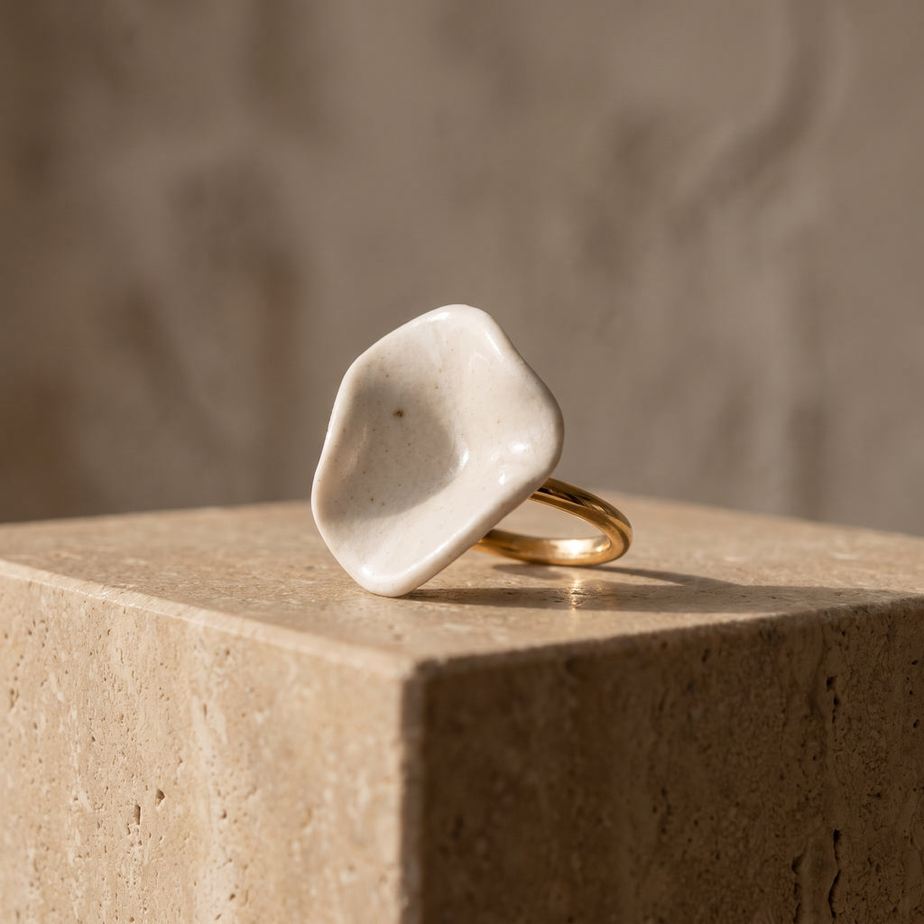 Pétalo Blanco — anillo de porcelana sobre superficie de travertino con luz cálida