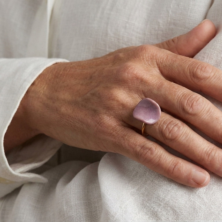 Pétalo Morado — anillo ajustable de porcelana lavanda mate con aro de oro en mano sobre pecho con camisa lino blanca, luz solar lateral cálida