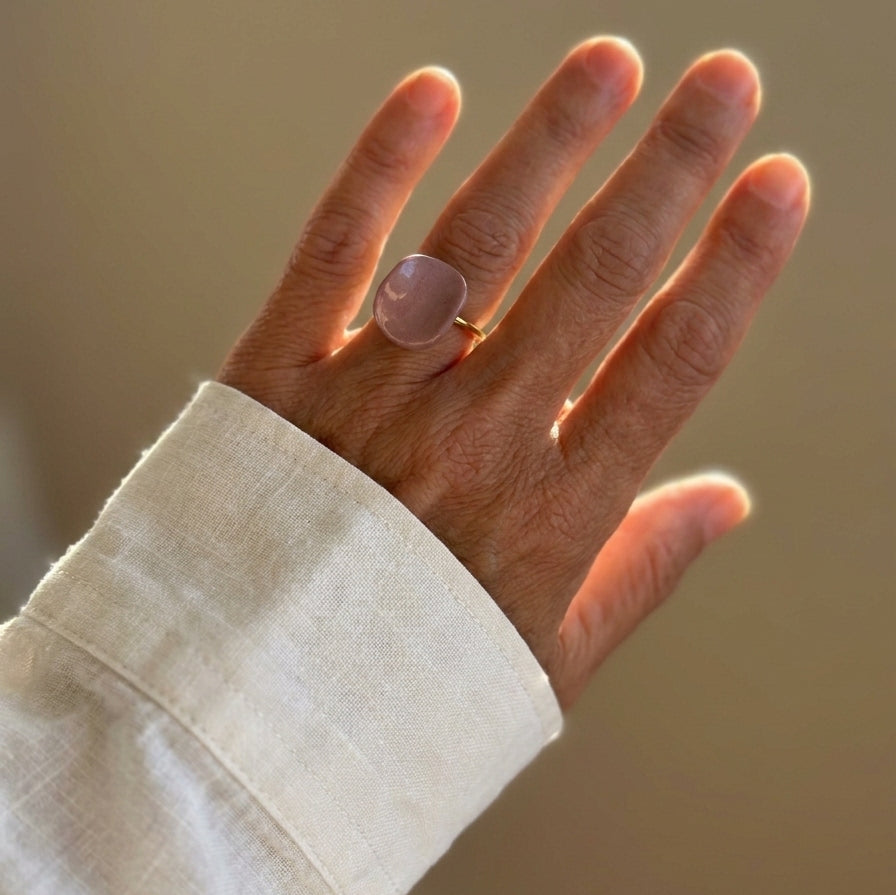 Pétalo Morado — anillo ajustable de porcelana lavanda mate con aro de oro en mano alzada con camisa lino blanca, luz dorada de atardecer sobre fondo tierra