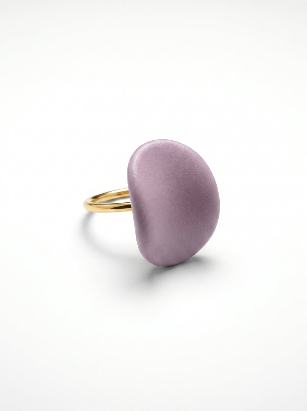 Pétalo Morado — anillo ajustable de porcelana lavanda mate con aro de oro en mano apoyada sobre superficie beige, vista cenital con luz natural