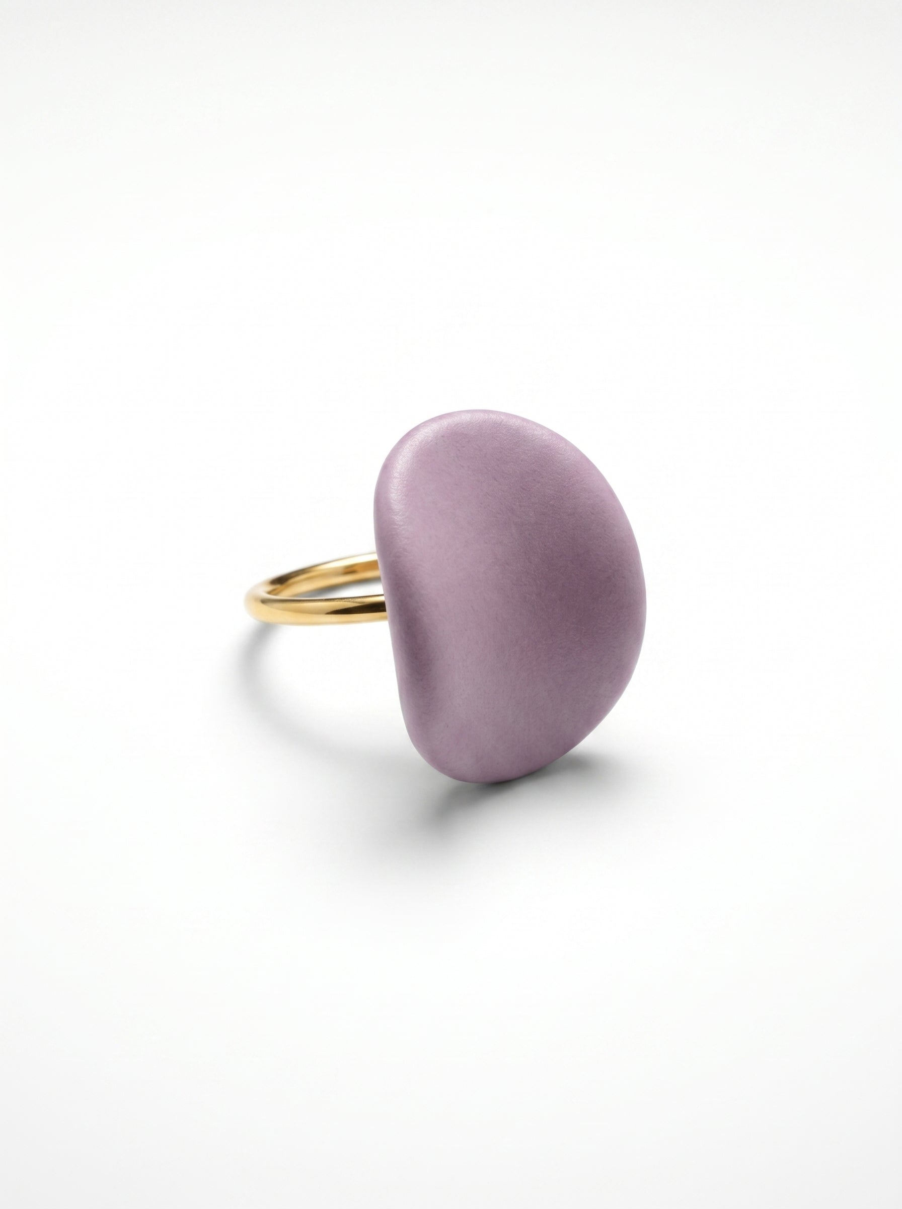 Pétalo Morado — anillo ajustable de porcelana lavanda mate con aro de oro en mano apoyada sobre superficie beige, vista cenital con luz natural