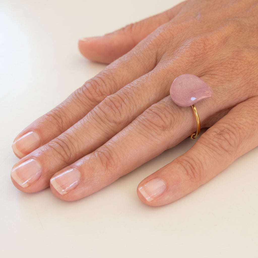 Pétalo Morado — anillo ajustable de porcelana lavanda mate con aro de oro en mano apoyada sobre camisa lino blanca, luz solar lateral con sombras suaves