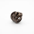 Peine Bronce — anillo de barro negro entrelazado sobre fondo blanco, vista cenital mostrando estructura de rollos y textura bronce