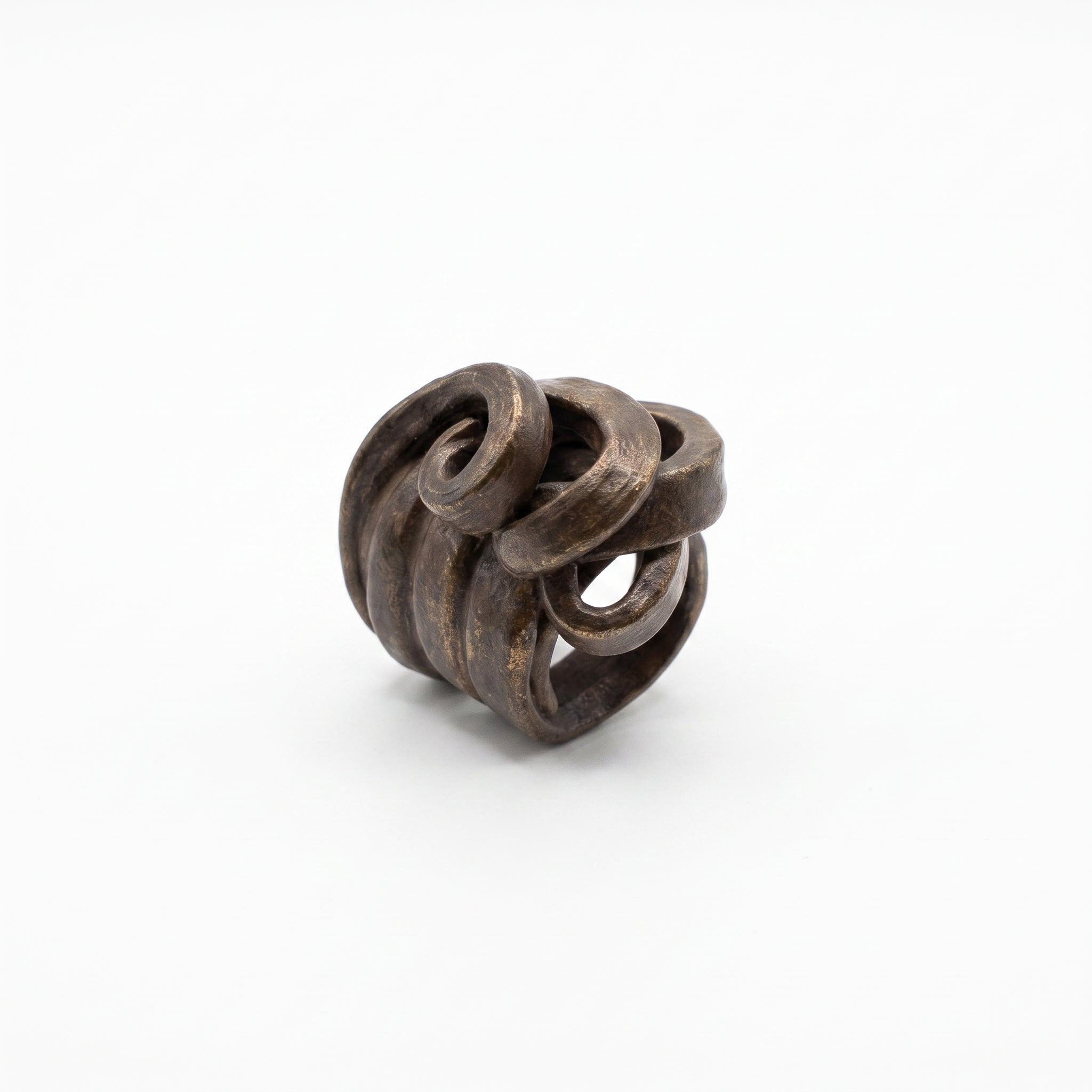 Peine Bronce — anillo de barro negro entrelazado sobre fondo blanco, vista cenital mostrando estructura de rollos y textura bronce