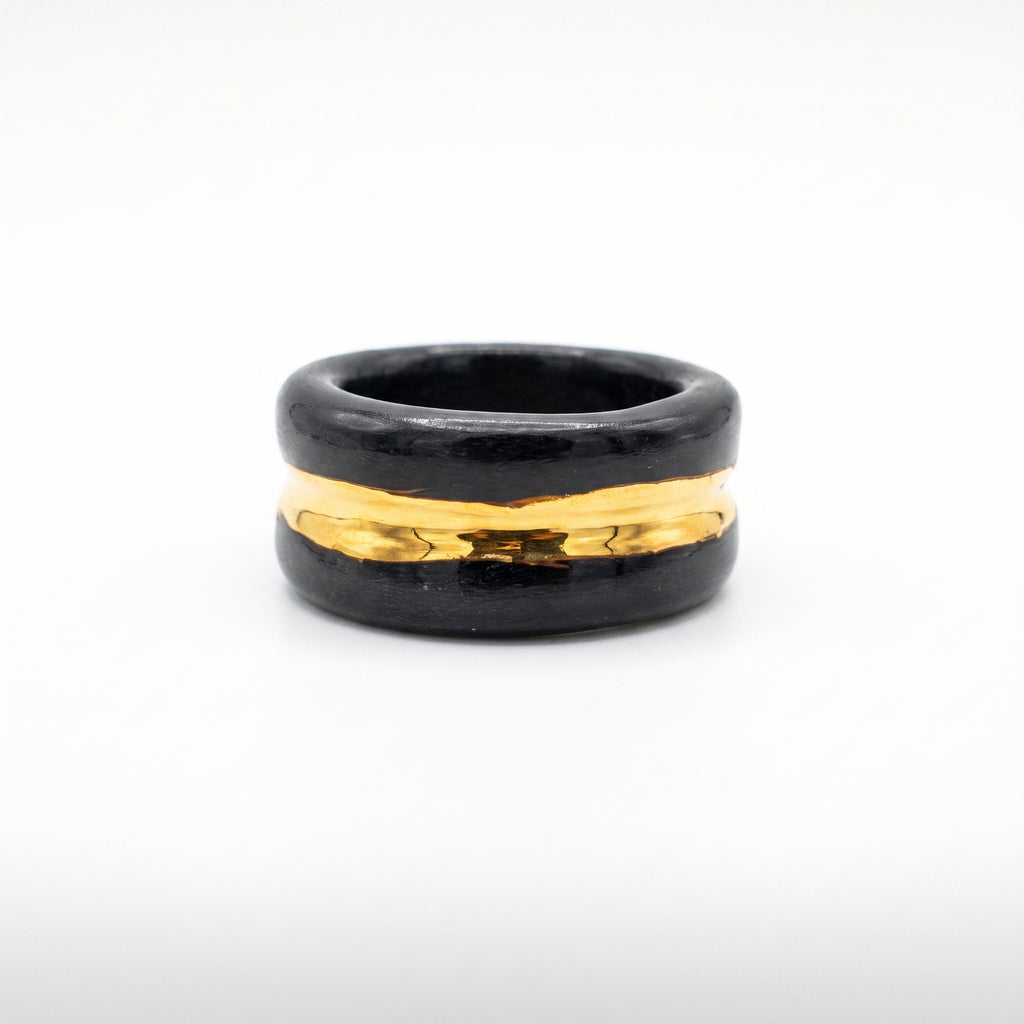 Trinity — anillo de porcelana negra con franja de oro central, vista frontal sobre fondo blanco mostrando la banda dorada brillante