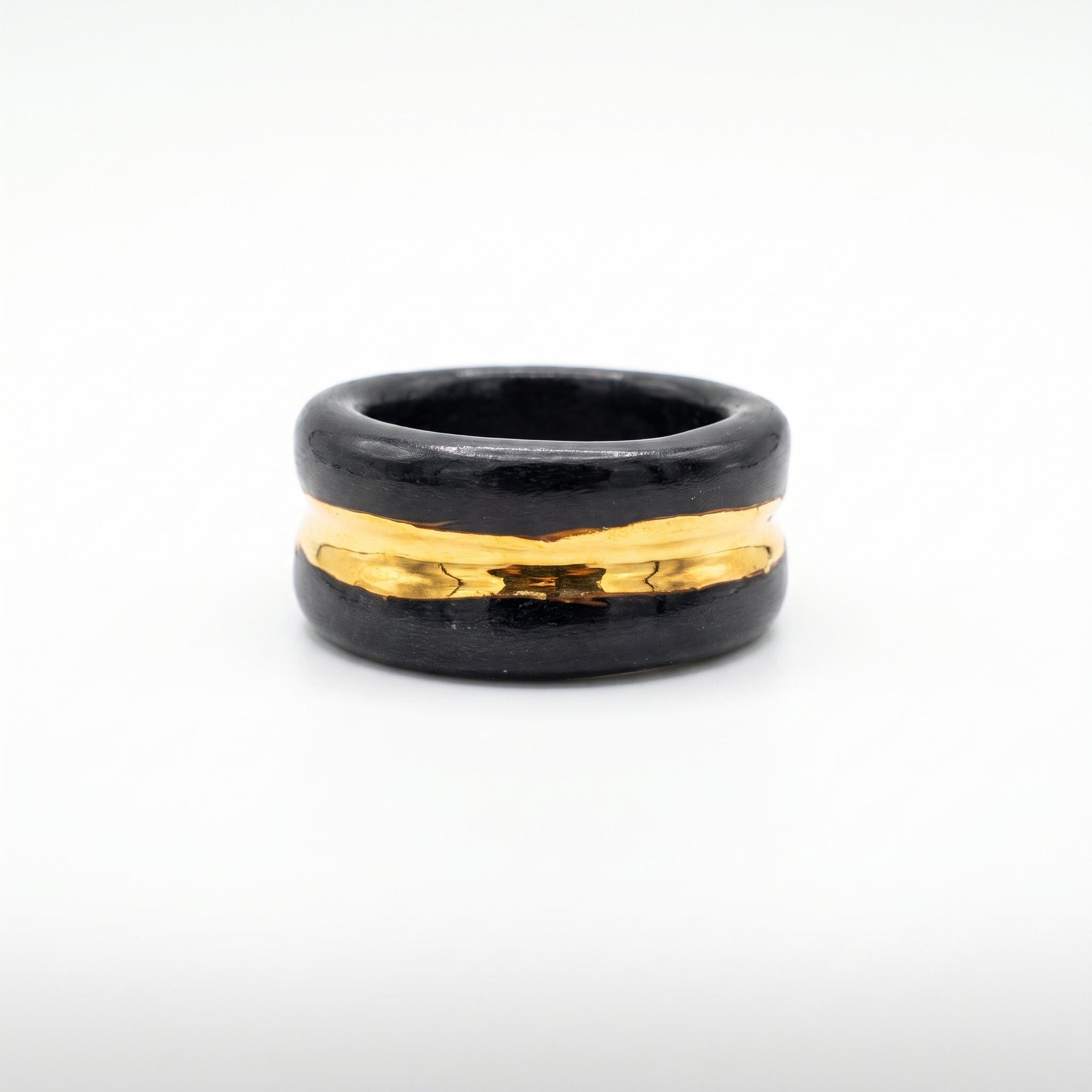 Trinity — anillo de porcelana negra con franja de oro central, vista frontal sobre fondo blanco mostrando la banda dorada brillante