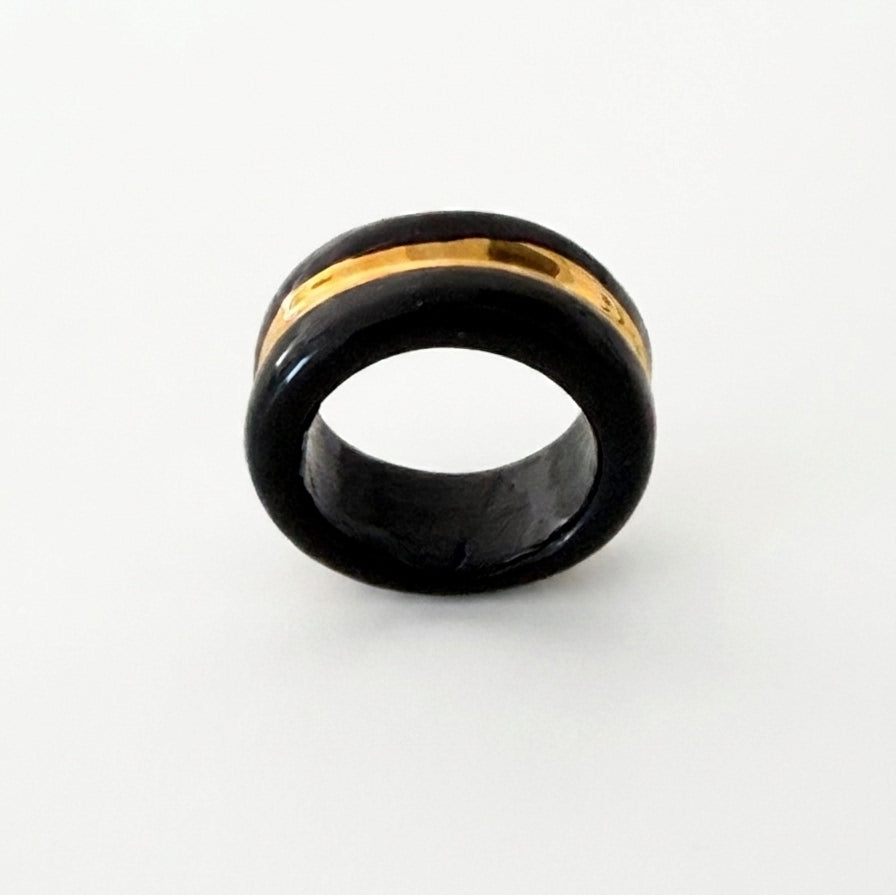 Trinity — anillo de porcelana negra con franja de oro central, vista lateral sobre fondo blanco mostrando el interior del aro y el grosor de la banda