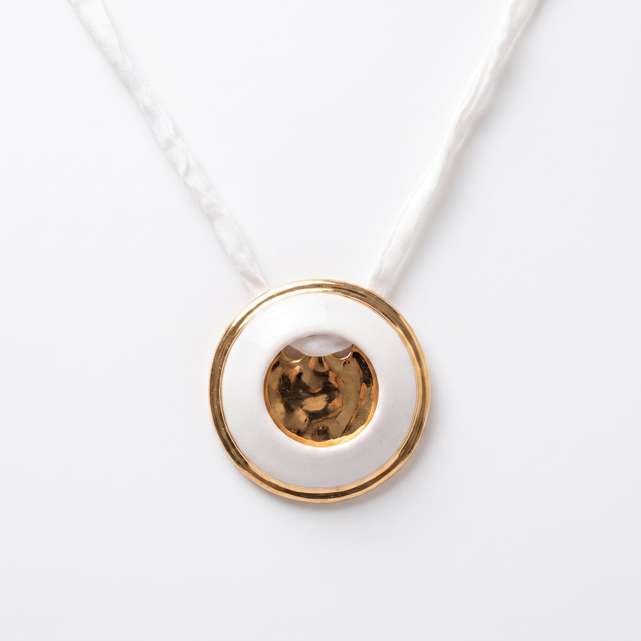 Eclipse Total colgante — disco de porcelana blanca con agujero central y aro de oro, vista frontal sobre fondo blanco con cordón de seda blanca trenzada mostrando la estructura círculo dentro de círculo