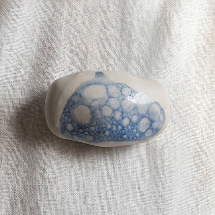 Espuma de Mar — anillo de porcelana blanca con mancha de esmalte azul y burbujas blancas, vista lateral sobre tela de lino natural