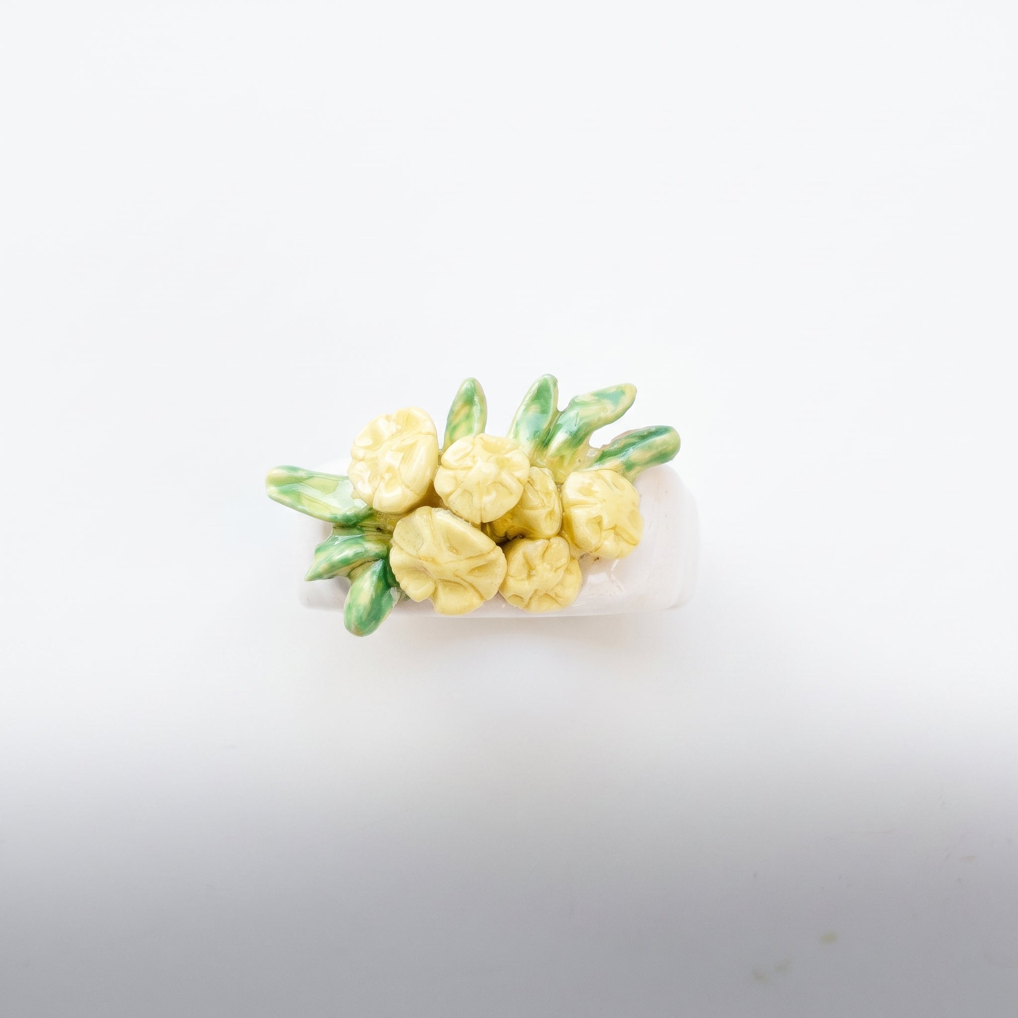 Bouquet Amarillo — anillo de porcelana con flores amarillo limón y hojas verdes modeladas a mano, vista cenital sobre fondo blanco