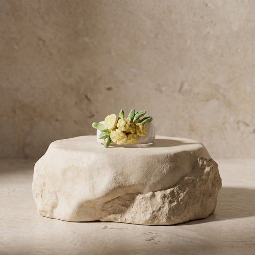 Bouquet Amarillo — anillo de porcelana con flores amarillo limón y hojas verdes modeladas a mano sobre piedra natural beige, fondo tierra cálido