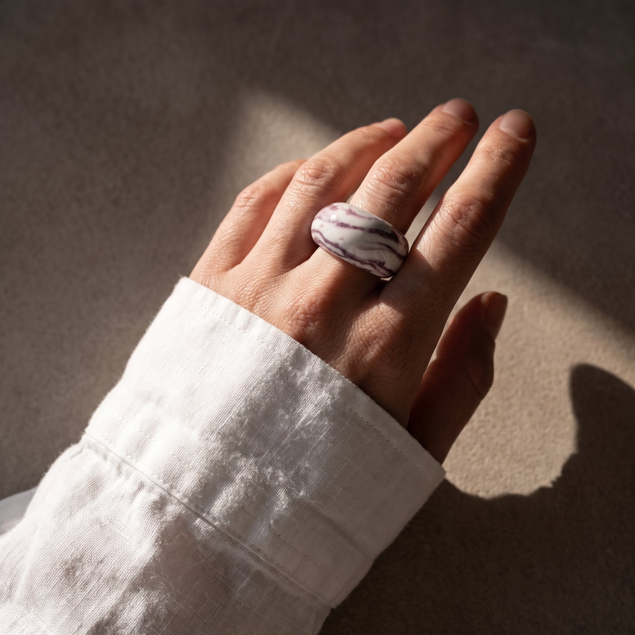 Petra Lilac — anillo de porcelana marmolada lila en mano con camisa blanca, luz solar