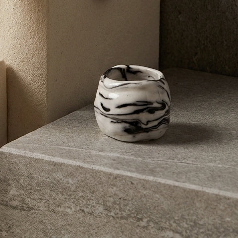 Petra Black — anillo de porcelana blanca con vetas negro intenso marmoladas apoyado sobre escalera de piedra beige, luz natural lateral