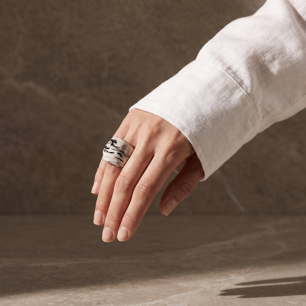 Petra Black — anillo de porcelana blanca con vetas negro intenso marmoladas a mano en mano caída con camisa blanca, fondo tierra oscuro