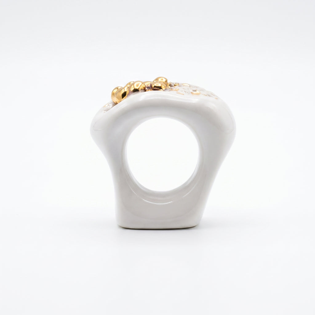 Navelgas — anillo de porcelana blanca con pepitas de oro irregulares, vista lateral mostrando la forma orgánica del aro sobre fondo blanco