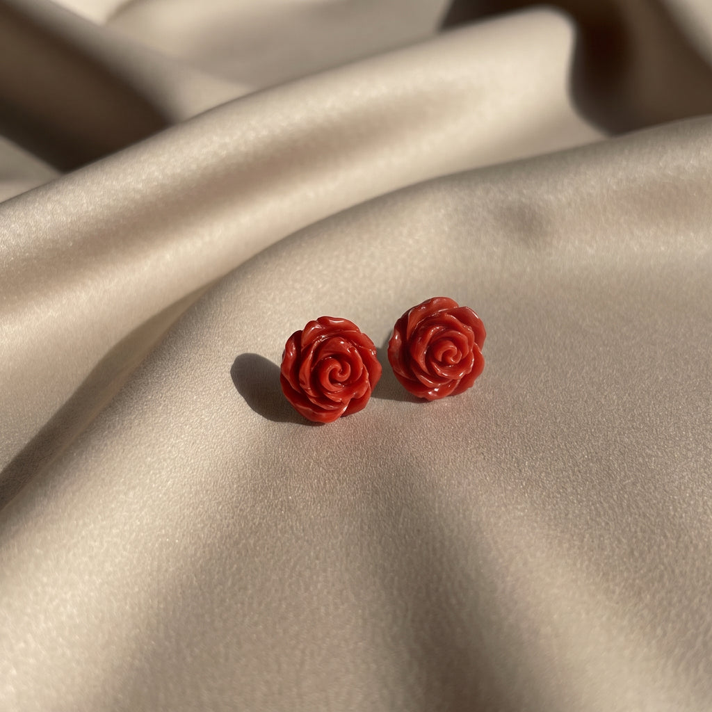 Pitimini Coral — pendientes de botón de porcelana coral sobre tela de seda champán en luz natural lateral, mostrando el color y la textura escultórica de los pétalos