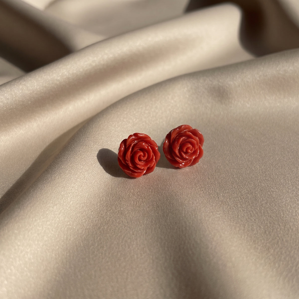Pitimini Coral — pendientes de botón de porcelana coral sobre tela de seda champán en luz natural lateral, mostrando el color y la textura escultórica de los pétalos