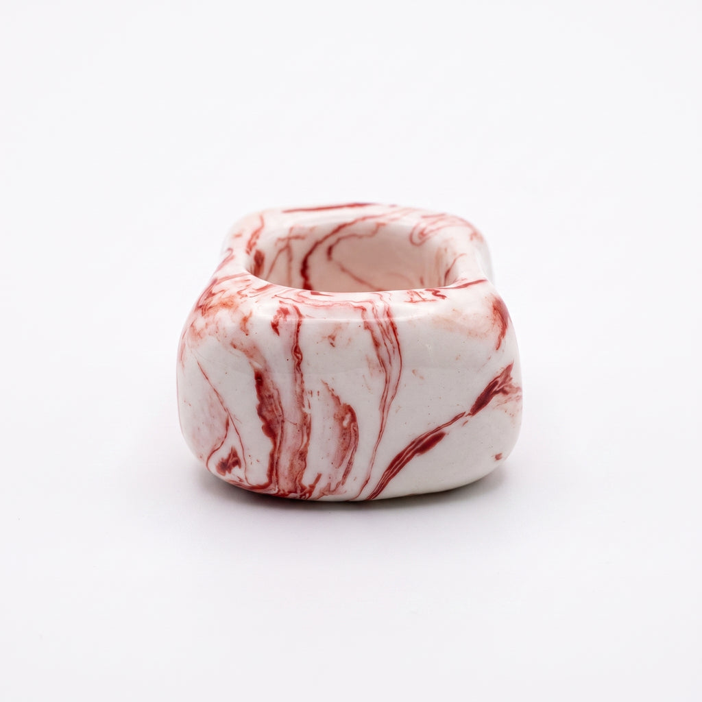 Petra Coral — anillo de porcelana blanca con vetas coral-rojo marmoladas, forma ancha y baja, vista lateral sobre fondo blanco