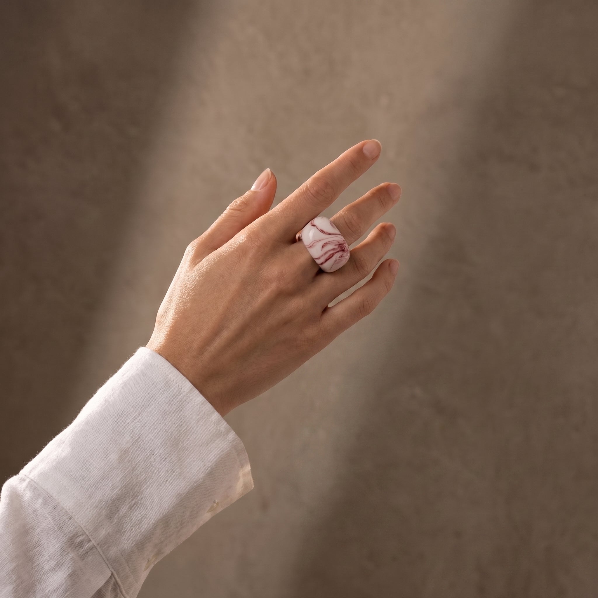 Petra Coral — anillo de porcelana blanca con vetas coral-rojo marmoladas en mano alzada con camisa blanca, fondo beige
